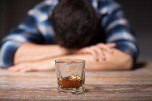 long-term effects of alcohol, alcoholism, alcohol addiction and people concept - male alcoholic with glass of whiskey lying or sleeping on table at night
