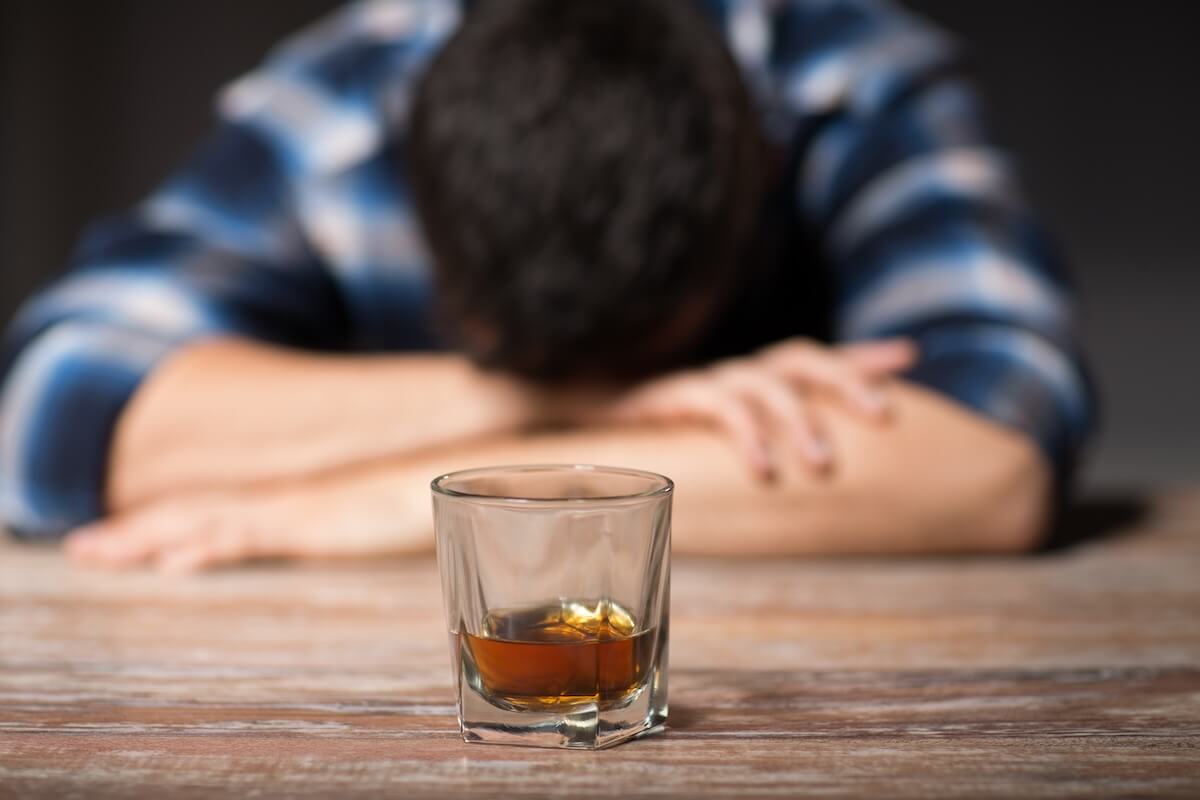 long-term effects of alcohol, alcoholism, alcohol addiction and people concept - male alcoholic with glass of whiskey lying or sleeping on table at night
