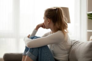 risk factors for addiction Side view young woman looking away at window sitting on couch at home. Frustrated confused female feels unhappy problem in personal life quarrel break