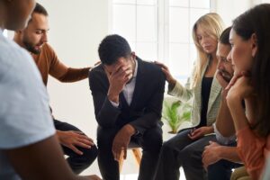 Should I Go To Rehab? Supportive friends comfort cheer unhappy male colleague feel depressed talk at counseling session. Caring people support unhappy distressed man group member. Psychological help, therapy concept.