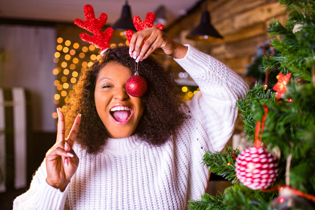 Joyful woman with antler headband on holding red Christmas ornament.
